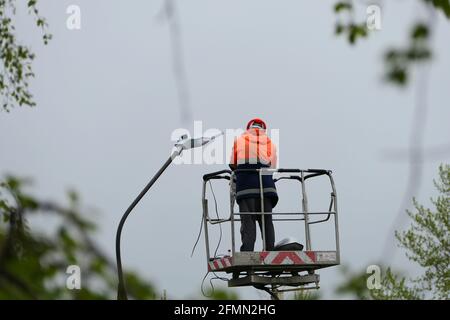 Ein Elektriker in Spezialkleidung und ein Helm repariert ein Straßenlaterne und Schrauben eine Straßenlaterne auf ein Stockfoto