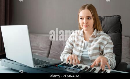 Frau lernt online Klavier zu spielen, indem sie einen Laptop im Innenraum verwendet. Frau spielt Instrument auf Synthesizer-Klavier während Online-Unterricht mit Lehrer. Online Stockfoto