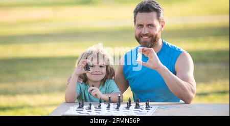 Sohn liegt auf Gras und spielt Schach mit Vater. Kind spielt Schach. Stockfoto