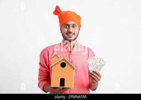 Home Loan Concept : Indischer Bauer hält handgemachtes Haus und Währung in der Hand Stockfoto