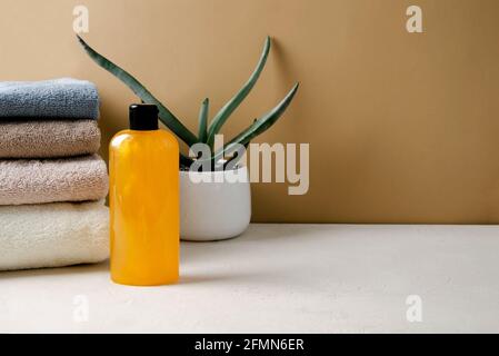 Shampoo, Gel, orangene Flüssigseife aus natürlichen Inhaltsstoffen in einer transparenten Flasche steht auf einem beigen Hintergrund neben einem Stapel beiger Handtücher, c Stockfoto