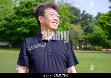 Porträt eines asiatischen Mannes mittleren Alters, der auf dem Rasen lächelt und ein T-Shirt trägt. Stockfoto