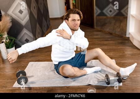 Müde, stilvoller Mann, der morgens zu Hause auf der Matte sitzt und trainiert. Gut aussehende männliche Training hart, um Körper Tanne und gesund zu halten, motiviert zu Stockfoto