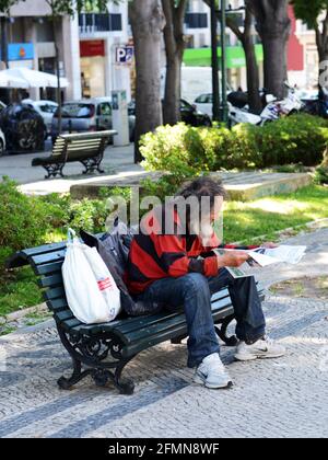 Ein Obdachloser, der auf einer Bank auf der Av. Da Liberdade in Lissabon, Portugal, sitzt. Stockfoto