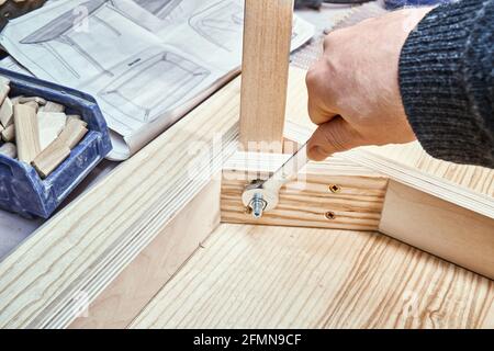 Gelernter Handwerker dreht Schraube auf Gelenkzwickel des Tisches aus Sperrholz, Furnier und massiver leichter Asche in Schreinerei-Werkstatt Nahaufnahme Stockfoto