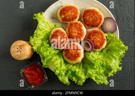 Saftig lecker überzogen mit Paniermehl und gebratenen Hähnchenschnitzel auf weißem Teller mit Gewürzen und Cetchup auf dunklem Hintergrund, Blick von oben. Stockfoto