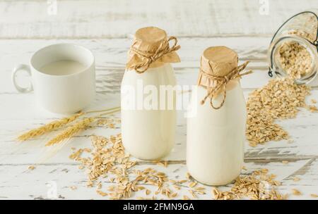 Hafermilch in Glasflaschen und Haferflocken in einer Tasse Auf einem Holztisch Stockfoto