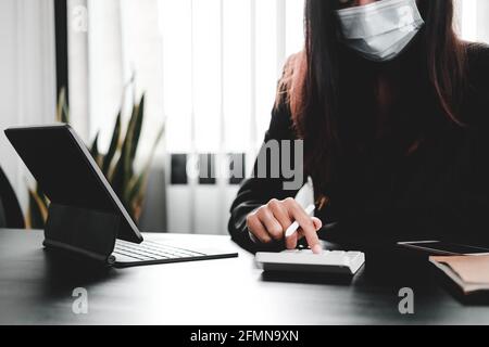 Geschäftsfrau tragen Maske arbeiten auf Schreibtisch Büro mit mit einem Rechner, um die Zahlen zu berechnen, Finanzen Buchhaltung Konzept. Stockfoto