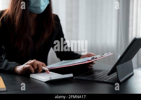 Geschäftsfrau tragen Maske arbeiten auf Schreibtisch Büro mit mit einem Rechner, um die Zahlen zu berechnen, Finanzen Buchhaltung Konzept. Stockfoto