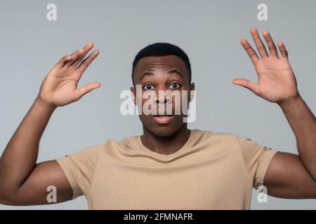 Überrascht junger Mann mit erhobenen Armen gestikuliert Stockfoto