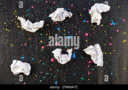 Chaotische Farbtropfen und Papierstücke auf schwarzer Textur. Gelbe, rote, blaue Punkte und Spritzer. Sechs zerknitterte Stücke weißes Papier. Abstraktes Multita Stockfoto