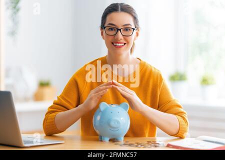 Frau sitzt am Schreibtisch mit Sparschwein. Konzept der Verwaltung des Familienbudgets. Stockfoto