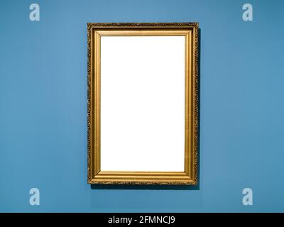 Vertikaler goldener Holzbildrahmen mit ausgeschnittem Canvas auf horizontaler Ebene Blaue Wand Stockfoto
