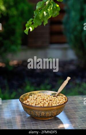 Schüssel mit gekochten Kichererbsen mit einem Holzlöffel auf dem Tisch im Freien. Gesundes vegetarisches Essen. Kopieren Sie die Spase. Stockfoto