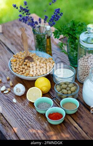 Eine Reihe von Zutaten für die Zubereitung von Hummus-Snacks: Kichererbsen, Tahini, Gewürze, Knoblauch, Petersilie, Olivenöl auf einem Holztisch. Rezept für ein Gemüse Stockfoto