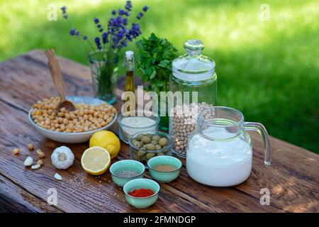 Eine Reihe von Zutaten für die Zubereitung von Hummus-Snacks: Kichererbsen, Tahini, Gewürze, Knoblauch, Petersilie, Olivenöl auf einem Holztisch. Rezept für ein Gemüse Stockfoto