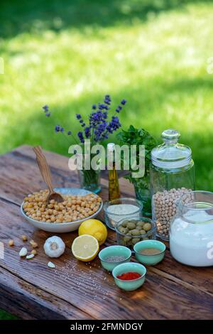 Eine Reihe von Zutaten für die Zubereitung von Hummus-Snacks: Kichererbsen, Tahini, Gewürze, Knoblauch, Petersilie, Olivenöl auf einem Holztisch. Rezept für ein Gemüse Stockfoto