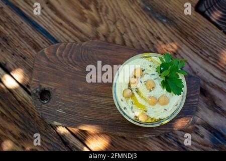 Klassische Hummus-Vorspeise aus Kichererbsen, Tahini, Olivenöl und orientalischen Gewürzen in einer Schüssel auf einem Holztisch. Traditioneller mediterraner vegetarischer Snack. Stockfoto
