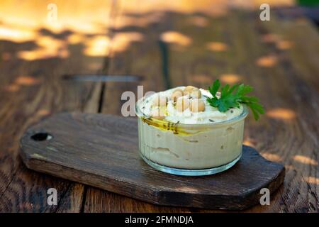 Klassische Hummus-Vorspeise aus Kichererbsen, Tahini, Olivenöl und orientalischen Gewürzen in einer Schüssel auf einem Holztisch. Traditioneller mediterraner vegetarischer Snack. Stockfoto