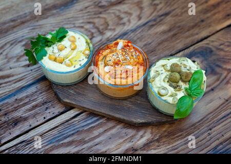 Drei Arten von klassischen Vorspeise Hummus mit Paprika und Knoblauch, Oliven, Kichererbsen, Tahini, Olivenöl, Und orientalische Gewürze in einer Schüssel auf einem Holztisch Stockfoto