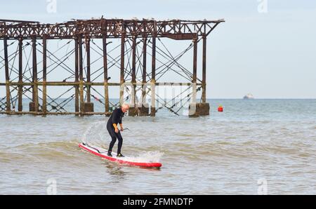 Brighton UK 11. Mai 2021 - EIN Paddle-Boarder versucht an einem warmen, sonnigen Morgen am verwelkten West Pier von Brighton die Brandung zu fangen, während heute eine Mischung aus Sonnenschein und Duschen für Großbritannien prognostiziert wird : Credit Simon Dack / Alamy Live News Stockfoto