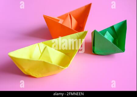 Drei bunte, bunte PapierOrigami-Boote in orange, gelb und grün auf einem rosa Hintergrund Stockfoto