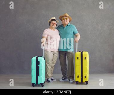 Glückliche Rentnertouristen in Sonnenhut und Brille mit Koffer stehen im Studio Stockfoto
