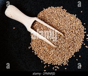 Draufsicht auf Holzschaufel auf einem Stapel von enthäuteten Scheunernyards Hirsekerne auf schwarzem Teller Stockfoto