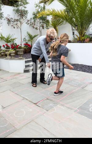 Eine Großmutter lehrt ihre Enkelin das traditionelle Spiel von hopscotch. Stockfoto