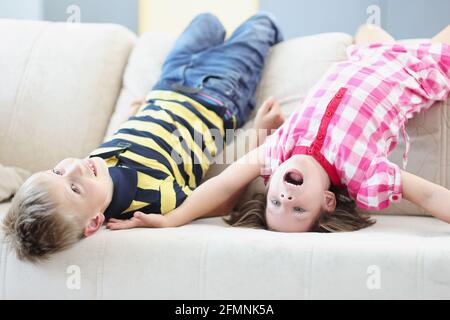 Kleiner Junge und Mädchen liegen auf der Couch auf dem Kopf Zu Hause Stockfoto