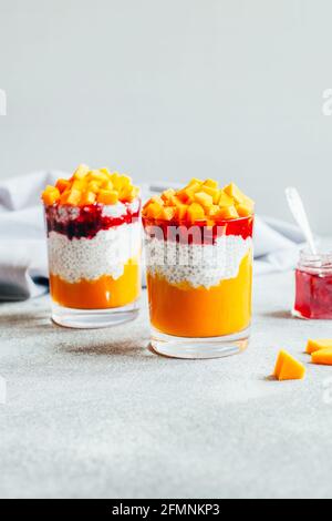 Nahaufnahme von zwei Gläsern mit Chia Pudding Kürbismus und Erdbeermarmelade auf grauem Hintergrund Stockfoto