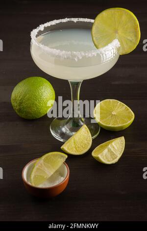 Draufsicht auf margarita Cocktailglas mit Limettenscheiben und Salz, auf Holztisch mit geschnittenen Limetten, vertikal Stockfoto