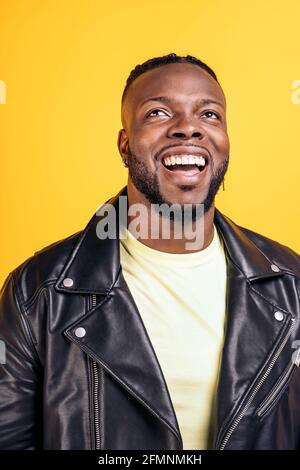 Fröhlicher schwarzer Mann in schwarzer Lederjacke, der im Studio vor gelbem Hintergrund lacht. Stockfoto