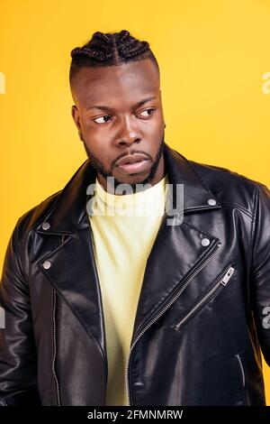 afroamerikanischer Mann mit cooler Frisur und schwarzer Lederjacke, der im Studio vor gelbem Hintergrund posiert. Stockfoto