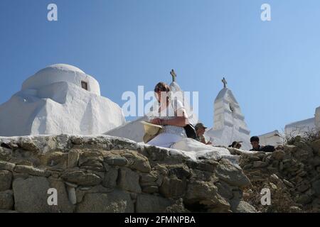 Mykonos Kirche von Panagia Paraportiani, Griechenland. 04 Oct 2017. Befindet sich in der Nähe von Kastro, in der Stadt. Eine reife Frau saß an der Wand vor der Kirche Stockfoto