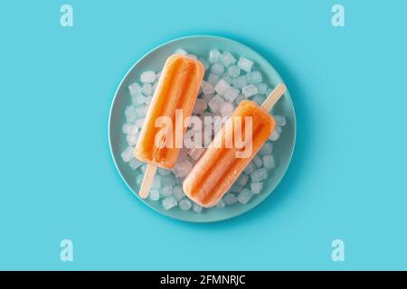 Orangefarbene Eiszapfen auf blauer Platte auf blauem Hintergrund Stockfoto