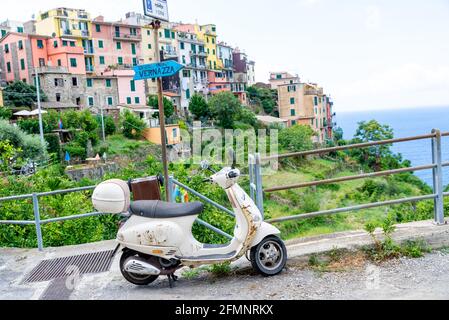 CORNIGLIA, ITALIEN - 27. Aug 2020: Ein weißer alter Roller, der auf einem Hang und im Hintergrund das Bergdorf Corniglia geparkt hat. Stockfoto