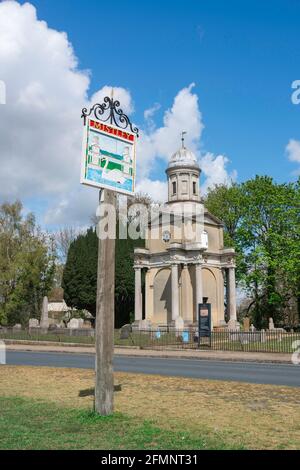 Mistley England, Blick auf das Dorfschild von Mistley auf dem Grün mit einem der beiden von Robert Adam entworfenen Türme aus dem Jahr 1776 Visible, Essex, Großbritannien Stockfoto