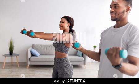 Positives afroamerikanisches Paar trainiert mit Hanteln zu Hause während der covid-19 Lockdown, Panorama Stockfoto