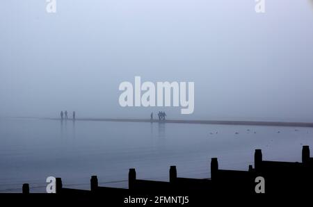 Menschen, die im Nebel auf der Street spazieren, einem Streifen aus Kiesel oder Sandbank, der sich bei Ebbe von Tankerton Beach, Whitstable, Kent, Großbritannien, ins Meer ausdehnt Stockfoto