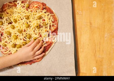 Childs Hand mit Pizza auf Backpapier zum Backen vorbereitet. Gesunde glutenfreie Pizza. Glutenfreier Kochkurs. Foto mit Kopierbereich. Stockfoto