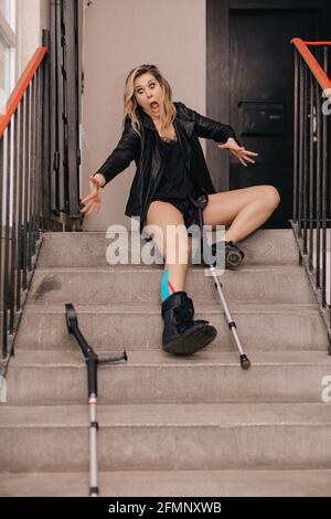 Junge Frau fiel auf Treppen. Gebrochenes Bein in einer Orthese und Krücken. Behinderte Person . Lebensversicherung Stockfoto