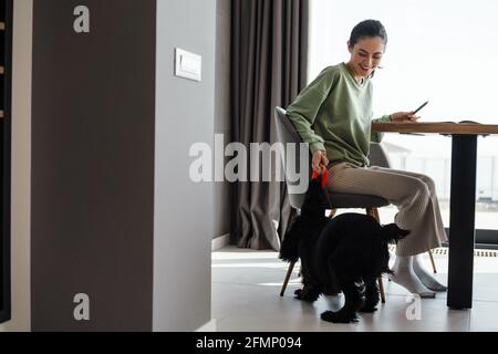 Glücklich junge Brünette Frau Streichelhund beim Sitzen an der Tisch im Innenbereich Stockfoto