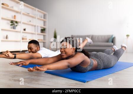 Sport während der covid Quarantäne. Millennial schwarzes Paar, das Yoga auf Sportmatten praktiziert und zu Hause Bogenasana macht Stockfoto