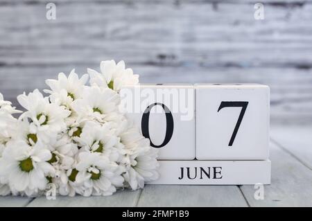 Weiße Holz-Kalenderblöcke mit dem Datum 7. Juni und weißen Gänseblümchen. Selektiver Fokus mit unscharfem Hintergrund. Stockfoto