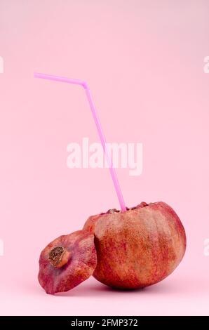 Granatapfel mit Stroh auf rosa Hintergrund. Natürliches Saftkonzept Stockfoto