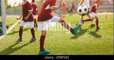 Kinder in Red Sport Trikot Shirts Jonglieren Fußballbälle auf Trainingseinheit an einem sonnigen Tag Stockfoto