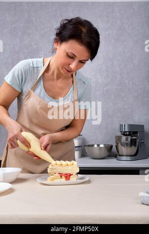 Die Küchenchefin schmückt Kuchen mit einer kulinarischen Tüte. Vertikaler Rahmen. Stockfoto