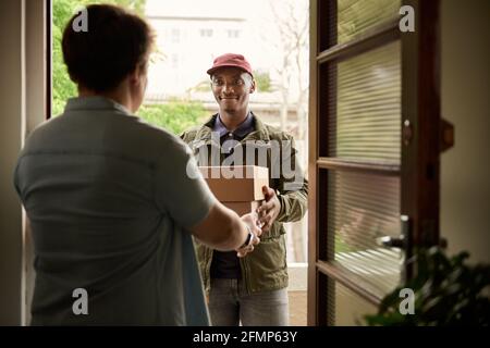 Afrikanischer Kurier lächelt, während er einem Kunden Pakete liefert Stockfoto