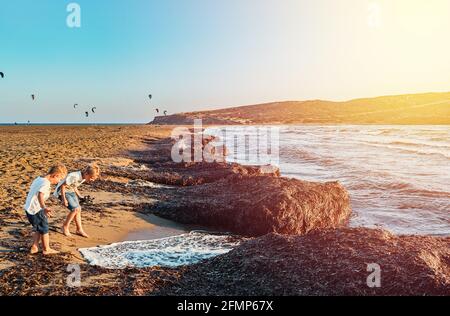 Kleine Barfußjungen, die mit Meereswellen spielen und Schaumstoff aufschäumen Sand Prasonisi Strand bei Sonnenuntergang am klaren Horizont in Griechenland Im Sommerabend Stockfoto